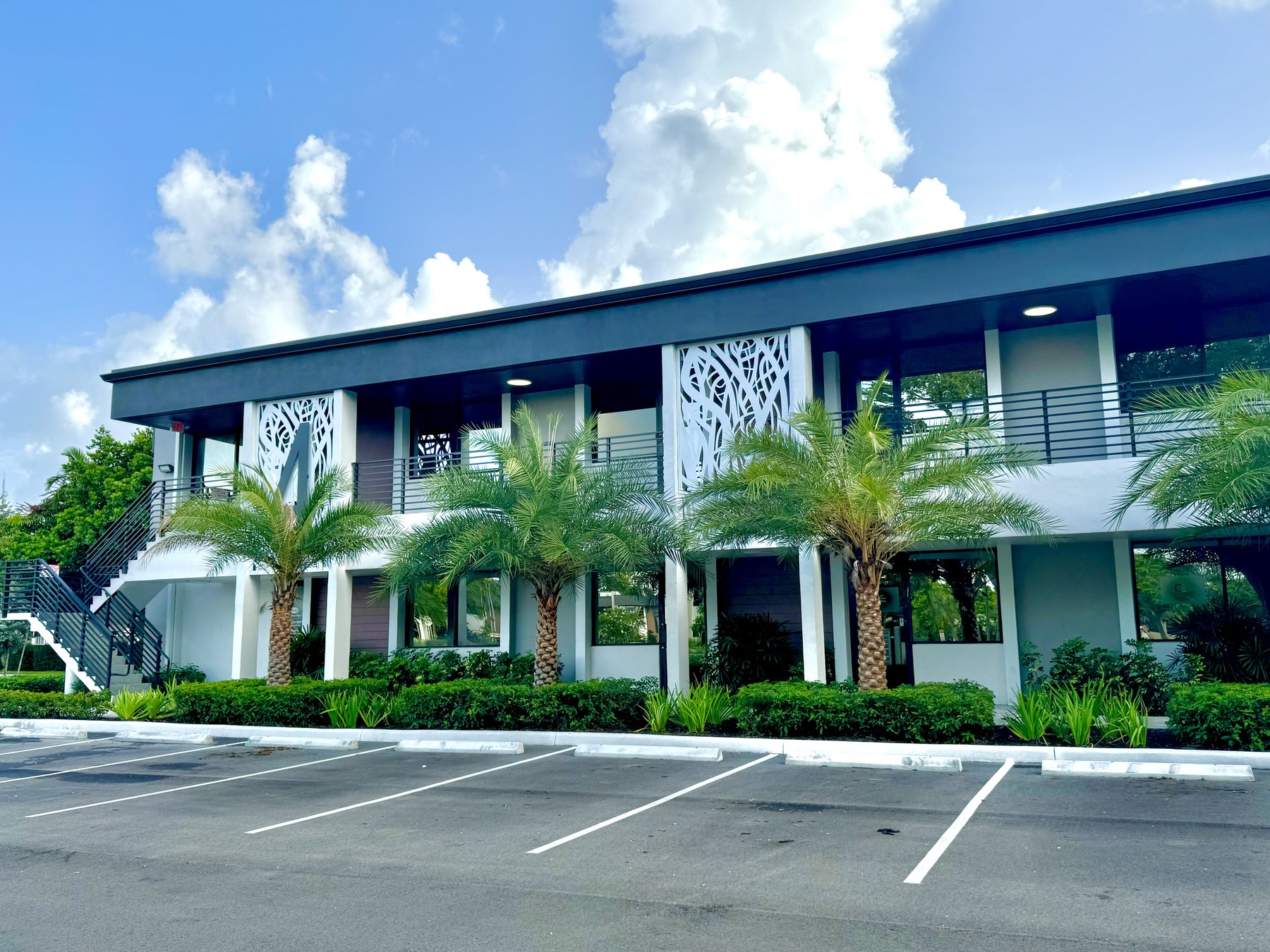 Sunlit exterior of an office building at the park with queen palms and open parking